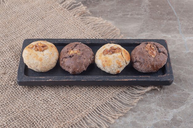 Cookies with walnut toppings on a small, black tray on marble