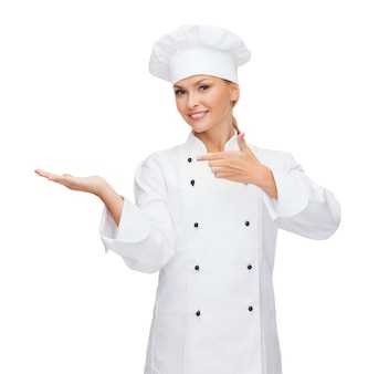 Концепция кулинарии, рекламы и еды - улыбающаяся женщина-повар, повар или пекарь, держащая что-то на ладони и указывающая на это пальцем
