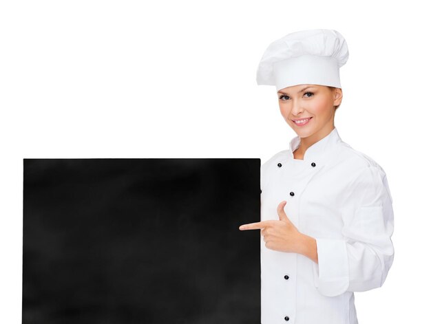 Кулинария, реклама и концепция питания - улыбающаяся женщина-повар, повар или пекарь, указывающая пальцем на белую пустую доску