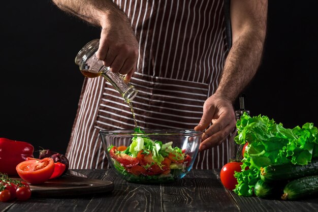 요리와 가정 개념 - 올리브 오일이 든 그릇에 샐러드 맛을 내는 남성의 손을 클로즈업하세요. 검은 배경에. 채식 음식, 건강 또는 요리 개념.