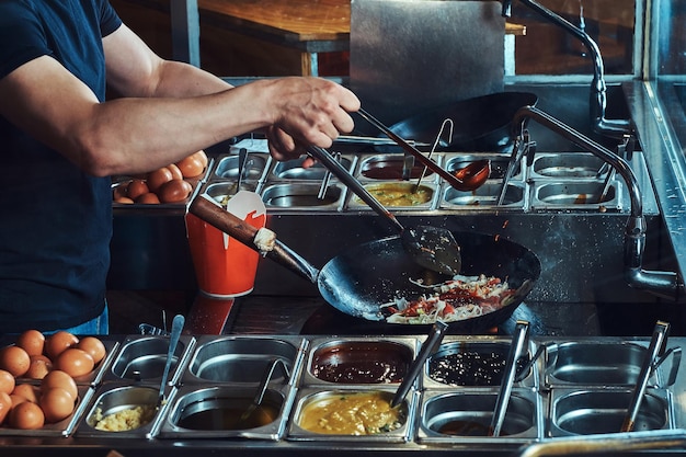 Процесс приготовления в азиатском ресторане. Кук жарит овощи со специями и соусом в воке