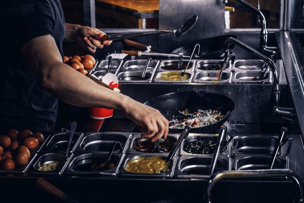 Процесс приготовления в азиатском ресторане. Кук жарит овощи со специями и соусом в воке