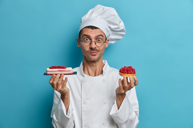 Cooking, profession, bakery concept. Young male cooker holds tasty confectionery, desserts decorated with berries