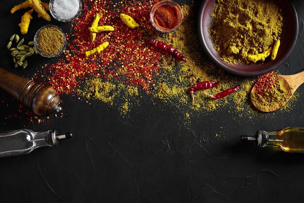 Free photo cooking using fresh ground spices with big and small bowls of spice on a black table with powder spillage on its surface, overhead view with copyspace. still life. flat lay. top view.