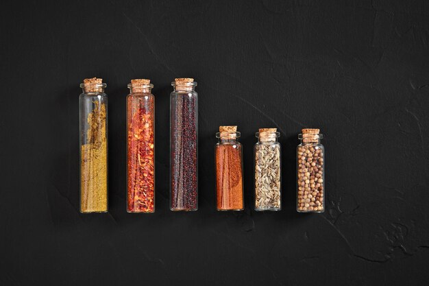 Cooking using fresh ground spices with six small jars of spice on a black table overhead view with copyspace. Still life. Flat lay. Top view.