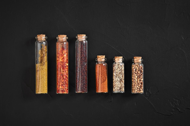 Cooking using fresh ground spices with six small jars of spice on a black table overhead view with copyspace. Still life. Flat lay. Top view.