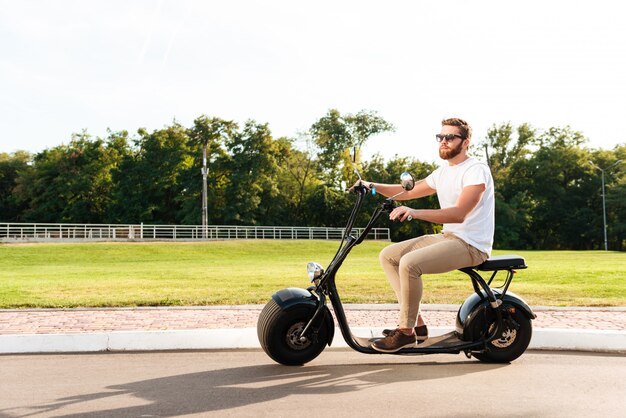 cool bearded man in sunglasses rides on modern motorbike outdoors