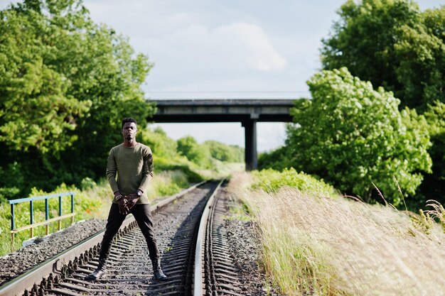 멋진 흑인 아프리카계 미국인 남자가 시골에서 철도를 걷고 포즈를 취합니다.