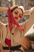 Free photo cool elegant stylish blonde lady with red lips in bright sunglasses silk blouse and beige trench coat looks down and poses outside