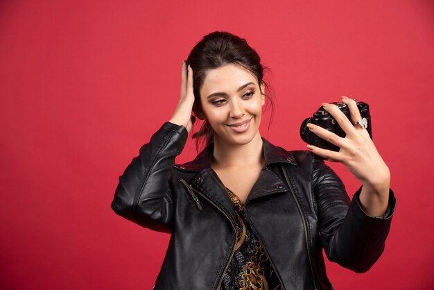 Cool girl in black leather jacket holding her professional camera and taking her selfies. 