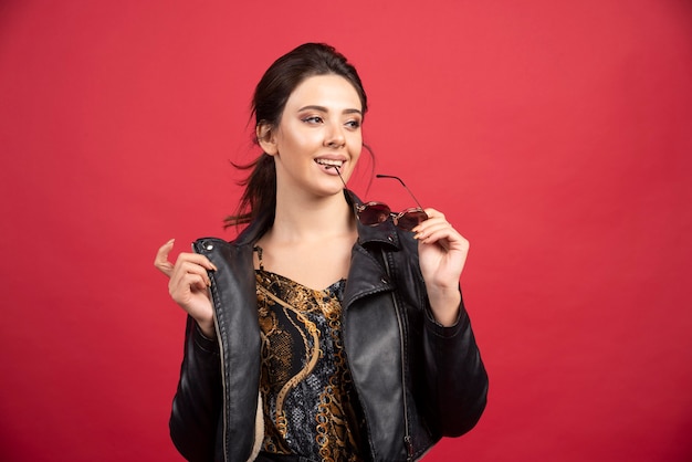 Cool girl in black leather jacket taking out her sunglasses and smiling. 