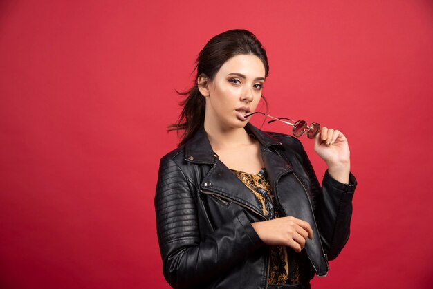 Cool girl in black leather jacket taking out her sunglasses and smiling. 