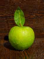 Free photo cool green apple with leaf on curved dark wood. side view.