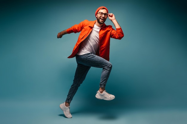 Cool guy in good mood posing on blue background and jumping