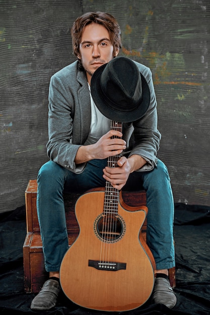 Cool guy sitting with guitar on gray space