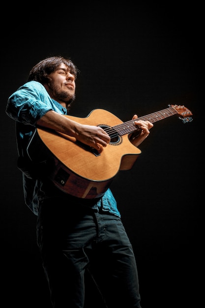 Cool guy standing with guitar on dark space