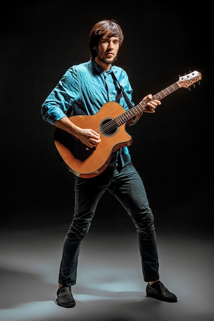 Cool guy standing with guitar on dark wall