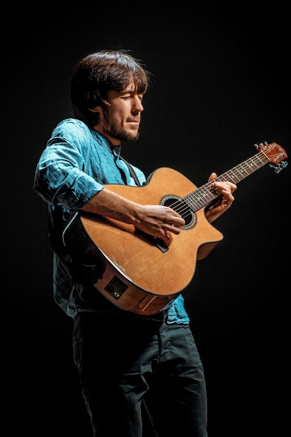 Cool guy standing with guitar on dark wall