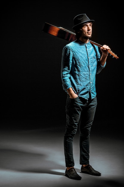 Free photo cool guy standing with guitar on dark wall