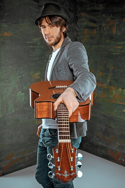 Cool guy standing with guitar on gray wall