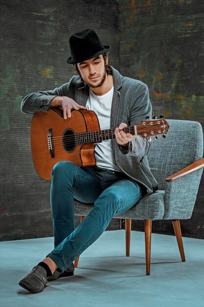 회색 공간에 기타를 연주하는 모자와 멋진 남자