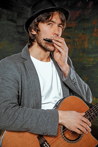 Крутой парень в шляпе играет на гитаре на сером