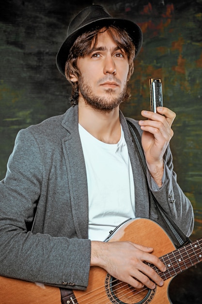 Free photo cool guy with hat playing guitar and harmonica on gray studio background