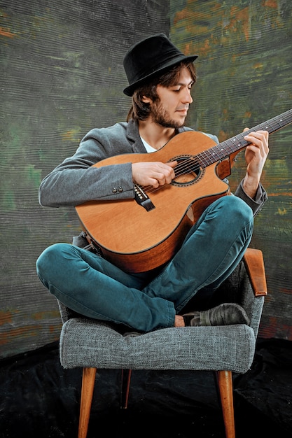 Бесплатное фото Крутой парень в шляпе играет на гитаре на сером