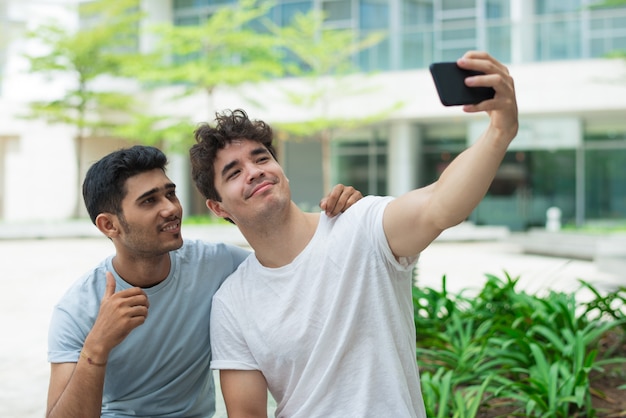 Cool handsome guys photographing on front camera of smartphone