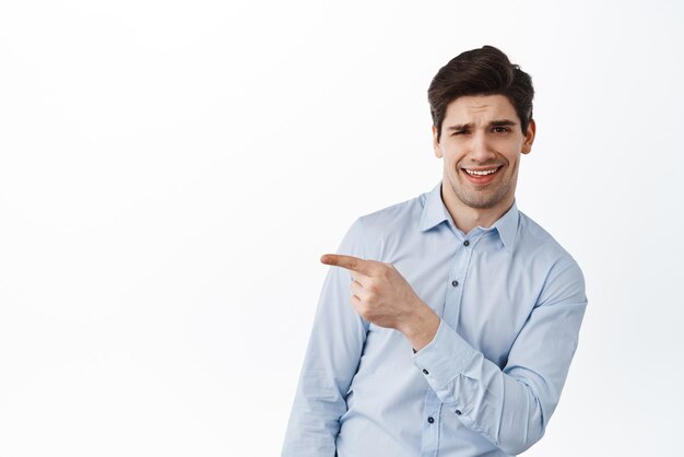 Cool and handsome young man in office clothes pointing aside at promo banner and smiling sassy showing logo promo text recommending something awesome white background