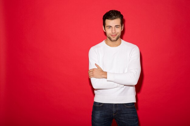 Cool smiling man in sweater looking with crossed arms over red wall