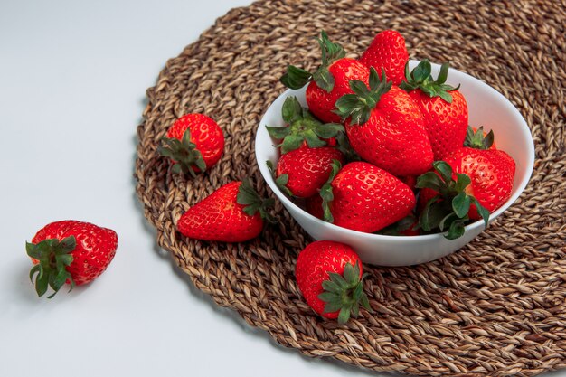 Cool strawberries in a white bowl on a grey gradient and round placemat background. side view.