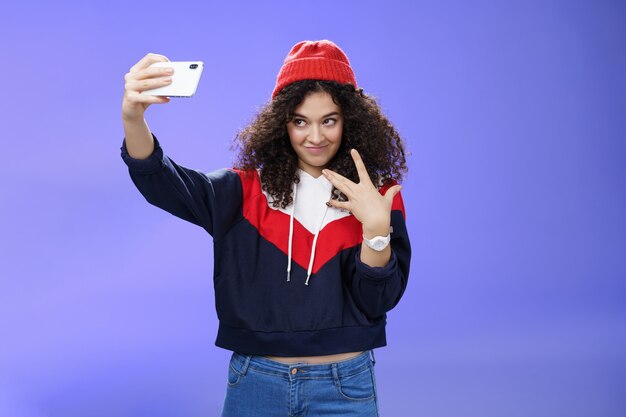 Cool and stylish goodlooking caucasian female with curly hair in trendy red beanie and sweatshirt lo...