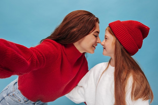 Cool trendy two sisters in red outfit looking at each other and makes photo on isolated background Smiling girls with long hair posing
