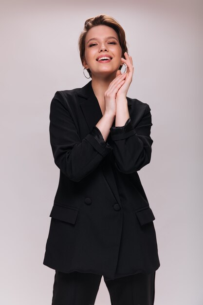 Cool woman in suit smiling on white background. Attractive lady in black jacket and pants poses on isolated backdrop