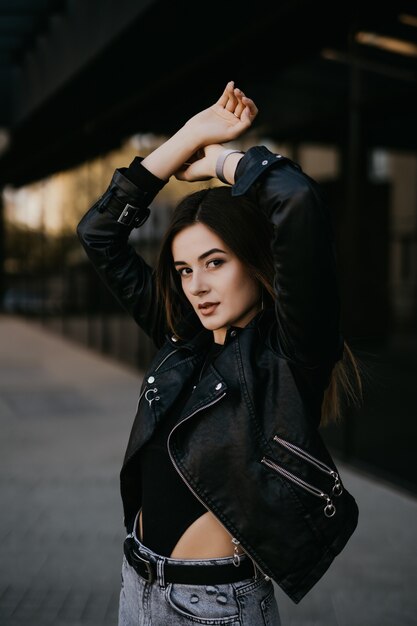 Cool young woman in stylish trench coat poses outside.