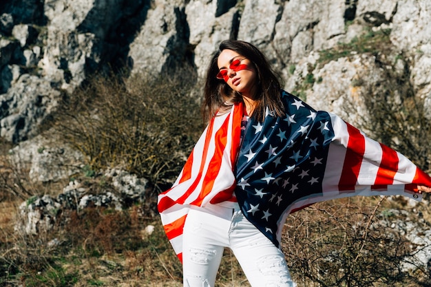 Cool young woman wrapped in flag standing in nature