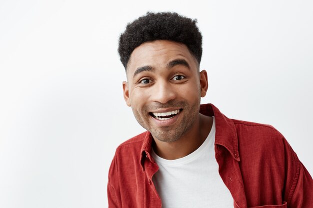 Copy space. Close up portrait of young attractive black-skinned cheerful happy man with afro hairstyle in casual white t-shirt and red shirt looking in camera with excited face expression.