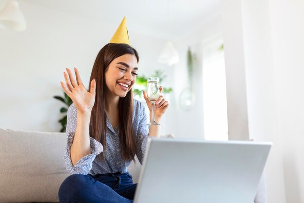 ビデオ通話で友人と誕生日のお祝いイベントをしている陽気な若い女性のスペースショットをコピー彼女はラップトップカメラに向かって白ワインのグラスでお祝いの乾杯をしています