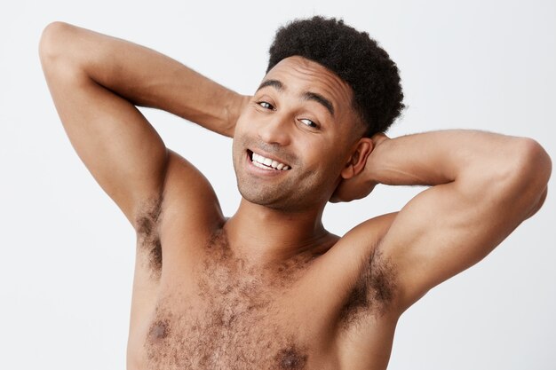 . Copy space. Spa, relaxation concept. Close up of cheerful attractive mature athletic dark-skinned man with afro hairstyle without clothes smiling, holding hands behind head.