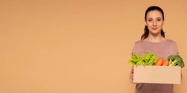 Free photo copy space woman holding cartoon box with vegetables