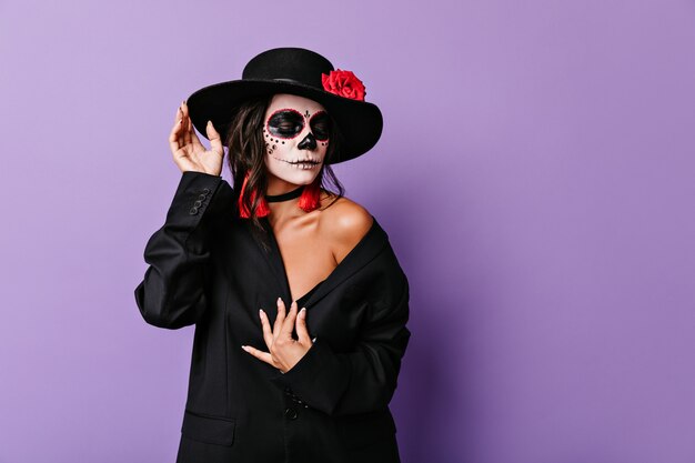 Кокетливая женщина опустила глаза, позирует в мафиозной одежде для портрета на Хэллоуин.