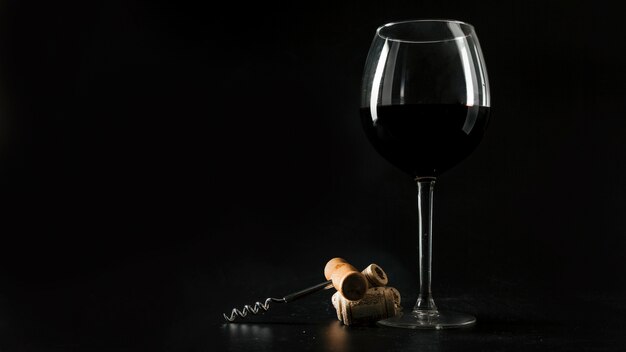 Corks and corkscrew near glass of wine