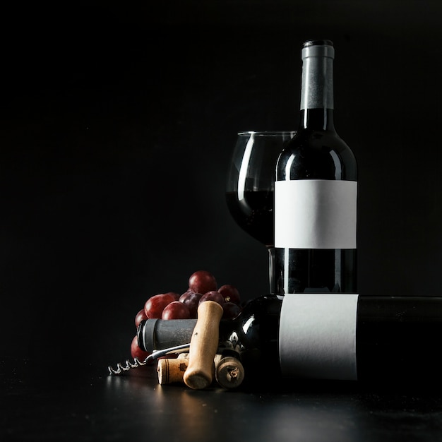 Corkscrew and grape near bottles and wineglass