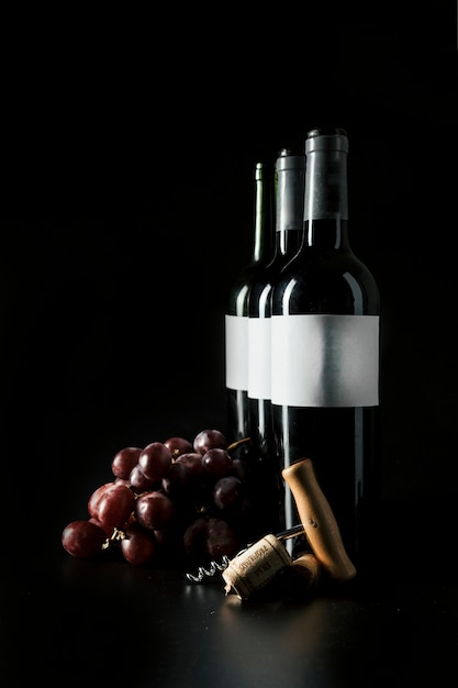 Corkscrew and grape near wine bottles