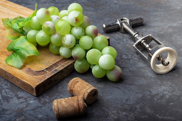 Corkscrew with green grapes on a wooden board