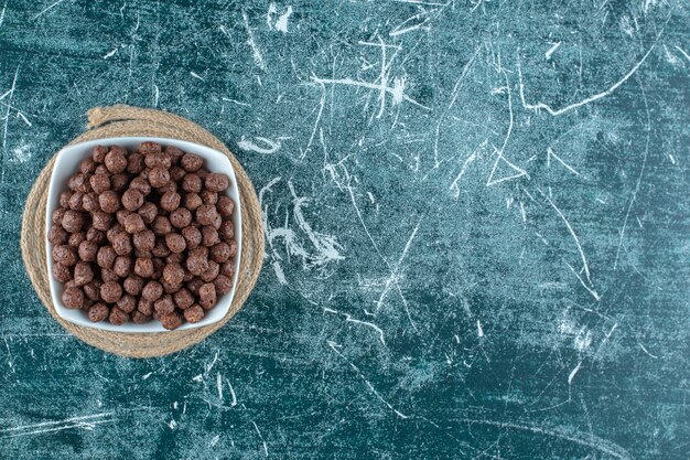 Corn balls in a bowl on a trivet , on the blue table. 