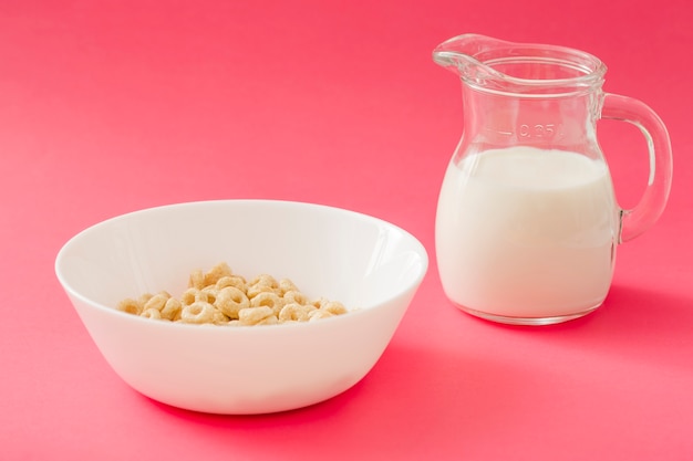 Free photo corn cereal rings in the bowl and milk jug over the pink background