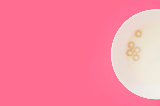 Corn cereal rings floating on the milk in the white bowl on pink background