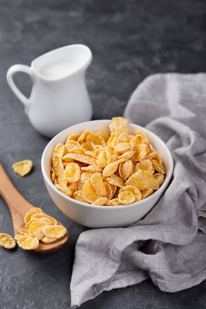 Corn flakes for breakfast in bowl with wooden spoon and milk